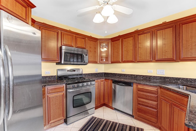kitchen with dark stone countertops, ceiling fan, light tile patterned floors, and stainless steel appliances