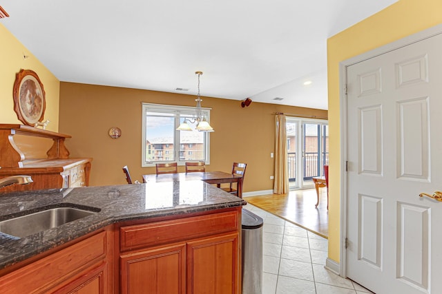 kitchen featuring a sink, hanging light fixtures, brown cabinets, light tile patterned floors, and visible vents