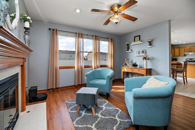 909 Revere St, Bourbonnais, IL 60914 - living area featuring baseboards, light wood-style flooring, a tiled fireplace, and a ceiling fan