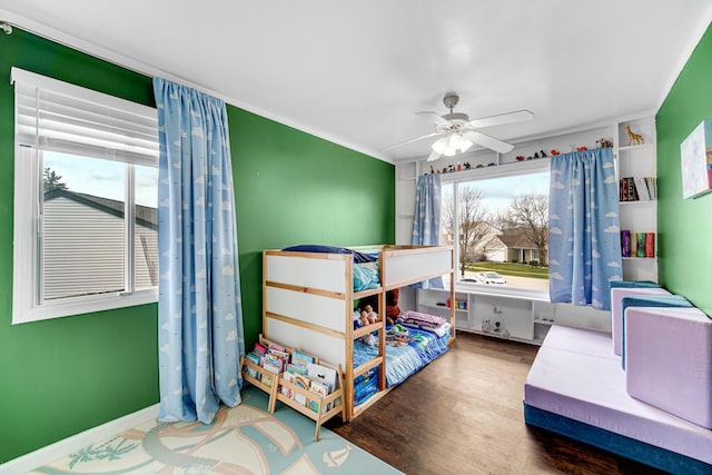 bedroom featuring ceiling fan, multiple windows, baseboards, and wood finished floors
