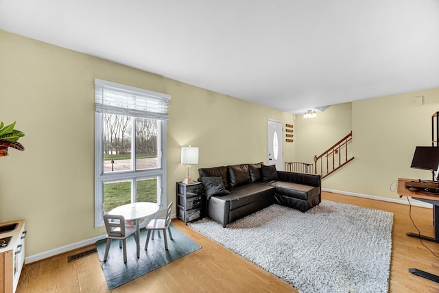 living room with light wood-type flooring, baseboards, visible vents, and stairway