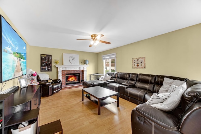 living room with light wood-style floors, ceiling fan, and a brick fireplace