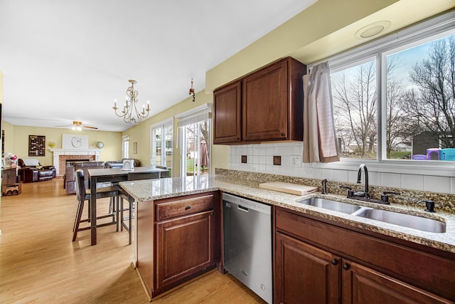 kitchen with tasteful backsplash, dishwasher, a sink, light wood-style floors, and a fireplace