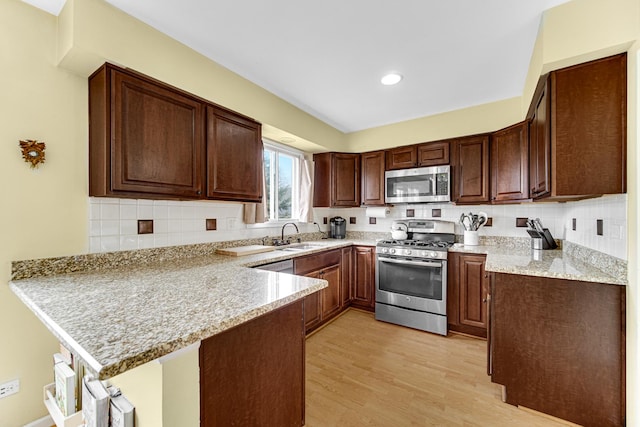 kitchen with a sink, a peninsula, stainless steel appliances, backsplash, and light wood-style flooring