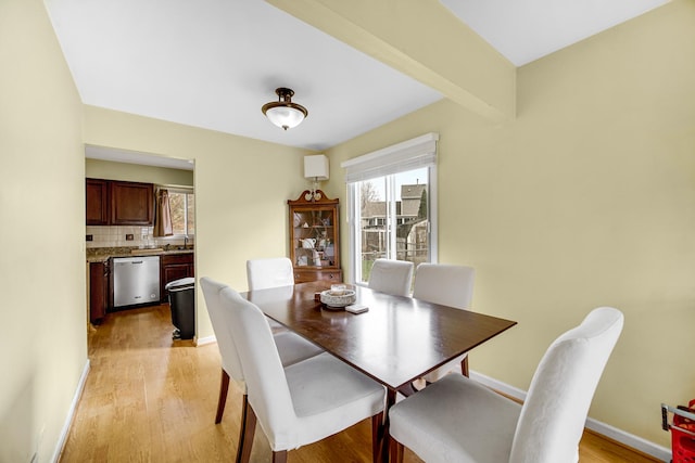 dining area featuring light wood-style flooring, beamed ceiling, and baseboards