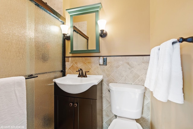 bathroom featuring toilet, vanity, tile walls, and wainscoting