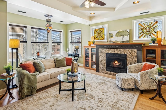 living room featuring a high end fireplace, wood finished floors, a tray ceiling, and visible vents