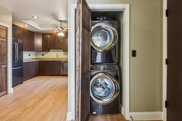 clothes washing area featuring stacked washer and clothes dryer, a sink, light wood finished floors, ceiling fan, and laundry area