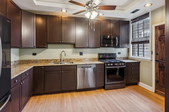 kitchen with a tray ceiling, a sink, light wood-style floors, visible vents, and appliances with stainless steel finishes