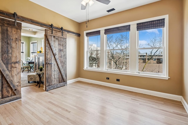 unfurnished room featuring baseboards, a barn door, visible vents, and light wood-style flooring