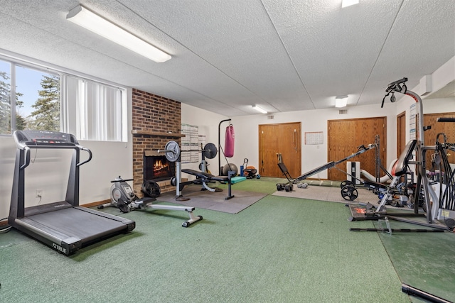 exercise room featuring carpet, a brick fireplace, and a textured ceiling