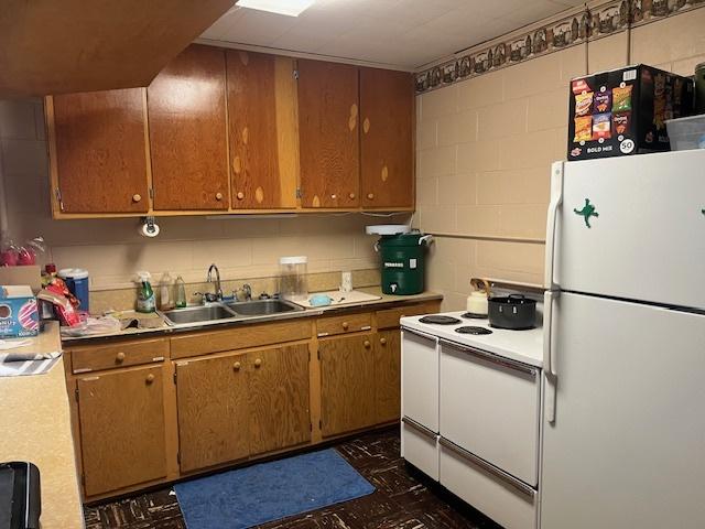 kitchen with concrete block wall, light countertops, a sink, and white appliances
