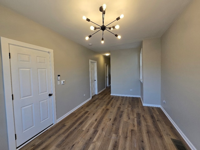 unfurnished room featuring baseboards, an inviting chandelier, and dark wood-style floors