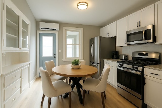 kitchen with light wood-style floors, a wall mounted air conditioner, white cabinets, backsplash, and stainless steel appliances