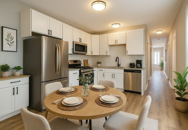 kitchen featuring white cabinets, a sink, light wood-style floors, stainless steel appliances, and decorative backsplash