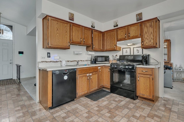kitchen featuring light countertops, a sink, brown cabinetry, under cabinet range hood, and black appliances
