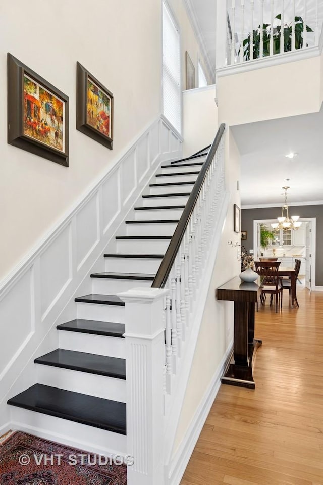stairs with a chandelier, crown molding, and wood finished floors