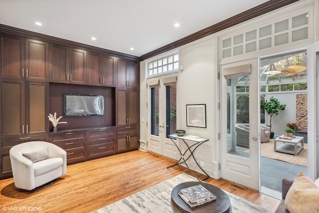 living room featuring plenty of natural light, light wood-style floors, ornamental molding, and french doors
