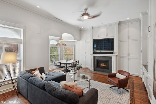 living room with crown molding, wood finished floors, recessed lighting, a ceiling fan, and a lit fireplace