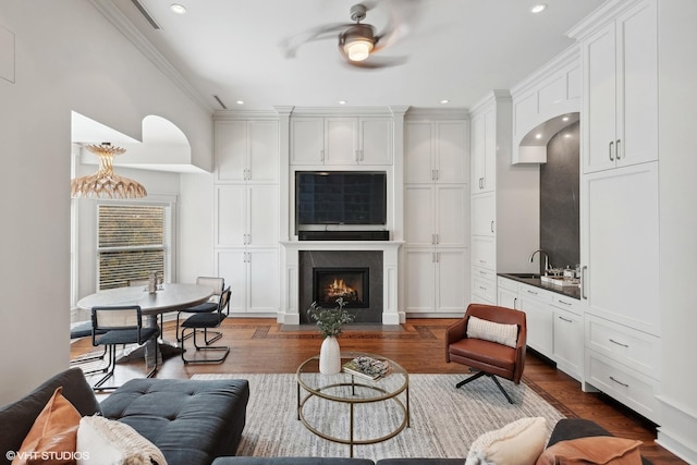 living room featuring a fireplace with flush hearth, dark wood-style flooring, crown molding, recessed lighting, and a ceiling fan