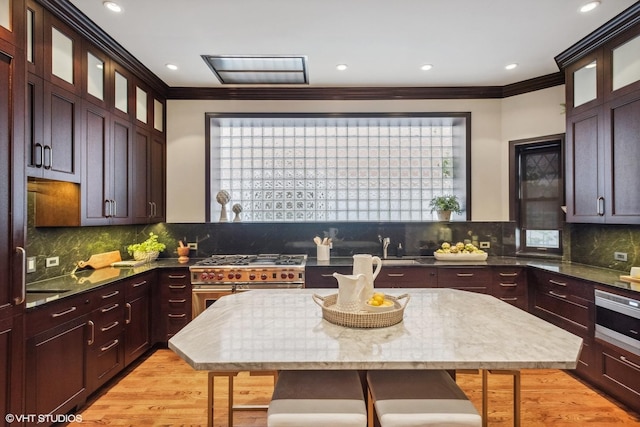 kitchen with a breakfast bar area, light wood finished floors, range with two ovens, and ornamental molding