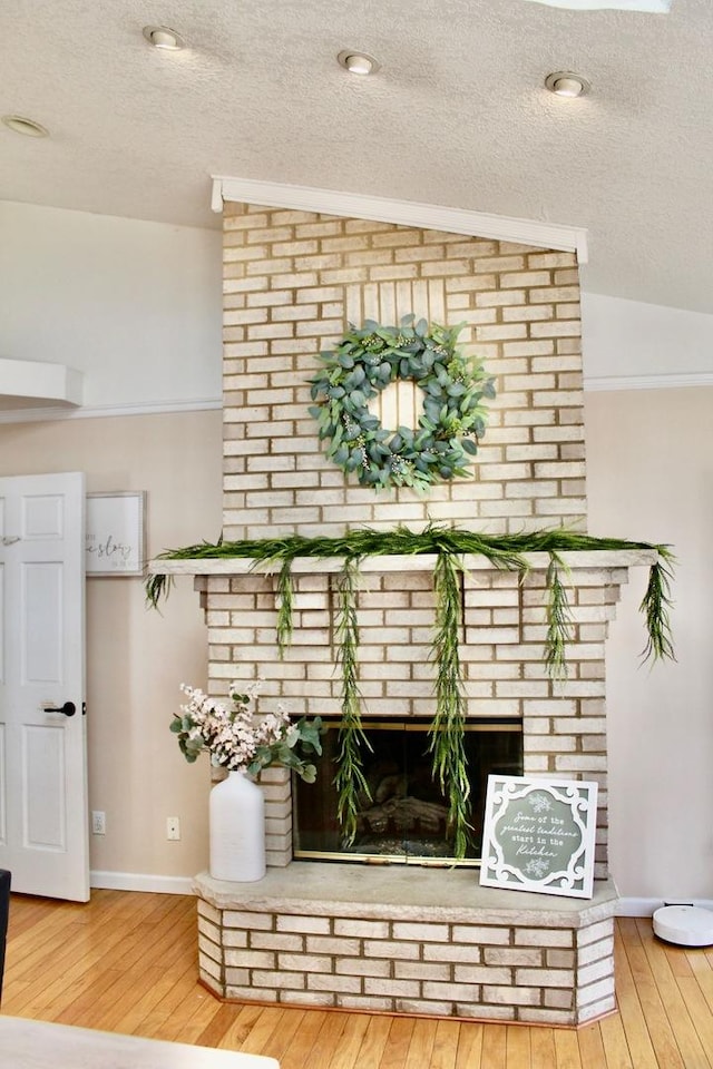 interior details featuring a brick fireplace, a textured ceiling, baseboards, and wood finished floors