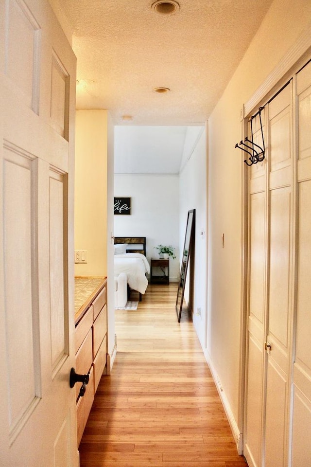 hall with light wood-style floors and a textured ceiling