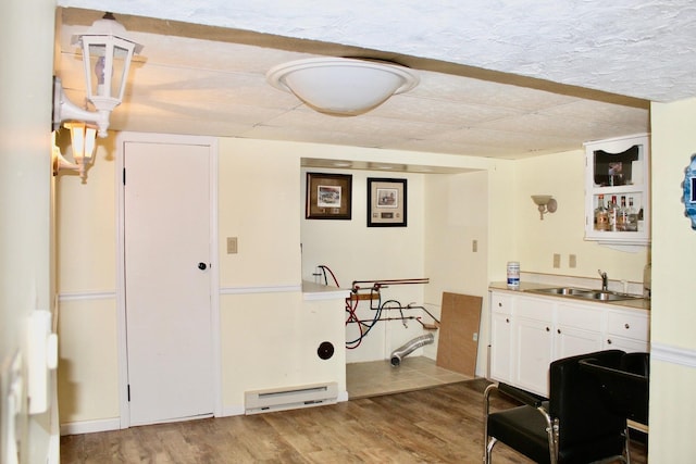 kitchen with light countertops, wood finished floors, white cabinetry, a sink, and a baseboard heating unit