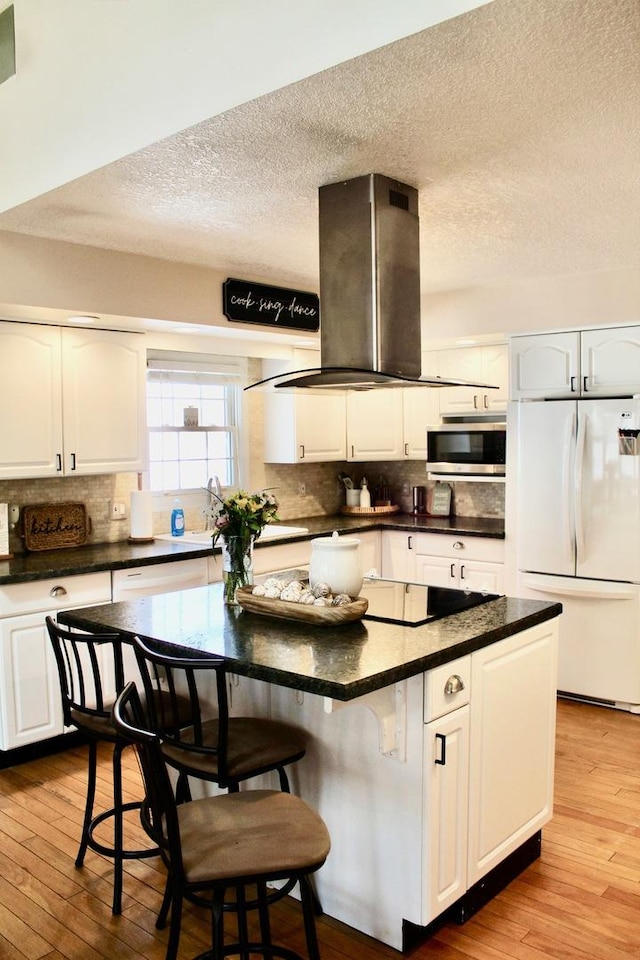 kitchen with hardwood / wood-style flooring, stainless steel microwave, island range hood, black electric stovetop, and freestanding refrigerator