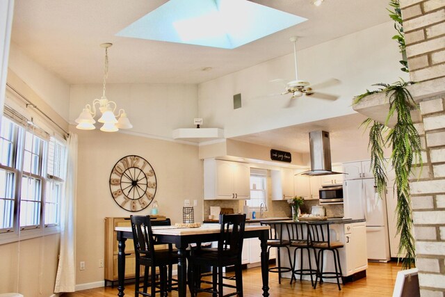 dining room with light wood finished floors, ceiling fan with notable chandelier, a skylight, and baseboards