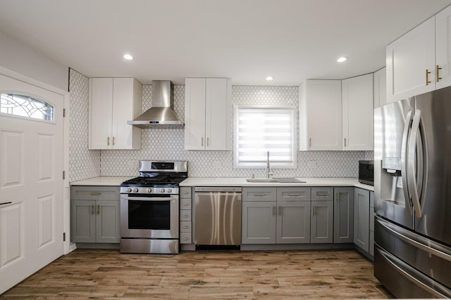 kitchen with gray cabinetry, wall chimney exhaust hood, a sink, and stainless steel appliances