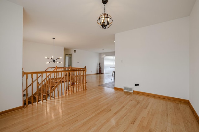 empty room with a chandelier, visible vents, wood finished floors, and baseboards