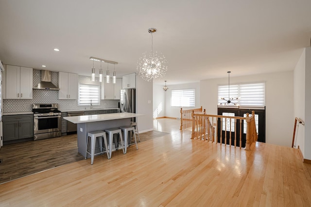 kitchen with tasteful backsplash, appliances with stainless steel finishes, a chandelier, wall chimney exhaust hood, and a wealth of natural light