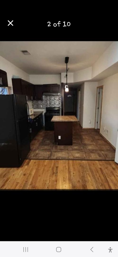 kitchen featuring visible vents, wood finished floors, a kitchen island, backsplash, and freestanding refrigerator
