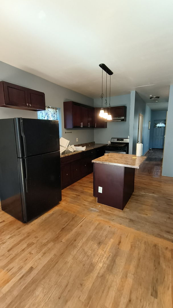 kitchen featuring dark brown cabinetry, a kitchen island, light wood finished floors, freestanding refrigerator, and stainless steel range oven