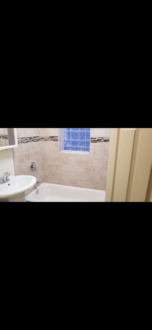 full bathroom featuring a bath, a sink, and tile walls