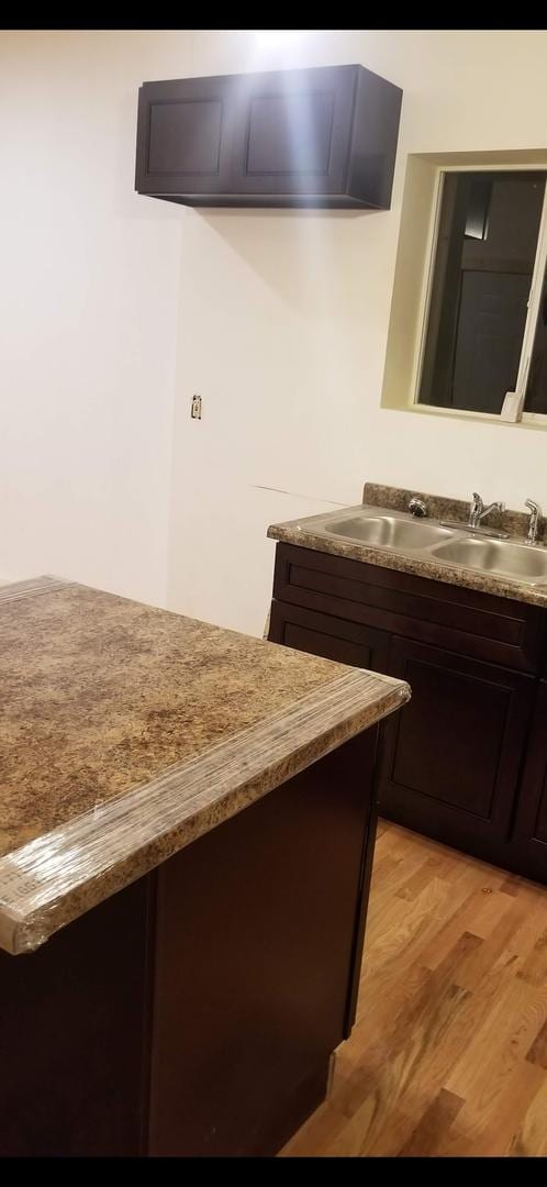 kitchen with light countertops, a sink, dark brown cabinetry, and light wood-style floors