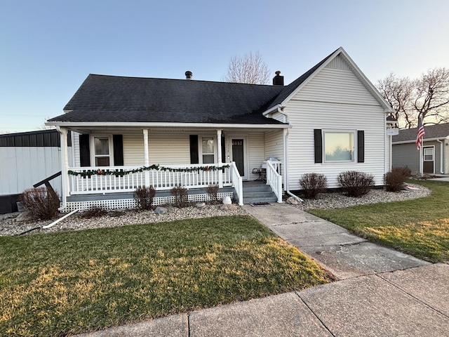 view of front of house featuring a front lawn, a chimney, a shingled roof, and covered porch