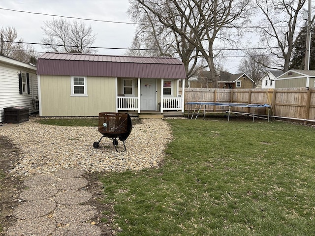 rear view of house with a trampoline, fence, a yard, and metal roof
