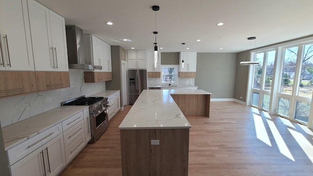 kitchen with a sink, a kitchen island, light wood finished floors, stainless steel appliances, and wall chimney range hood