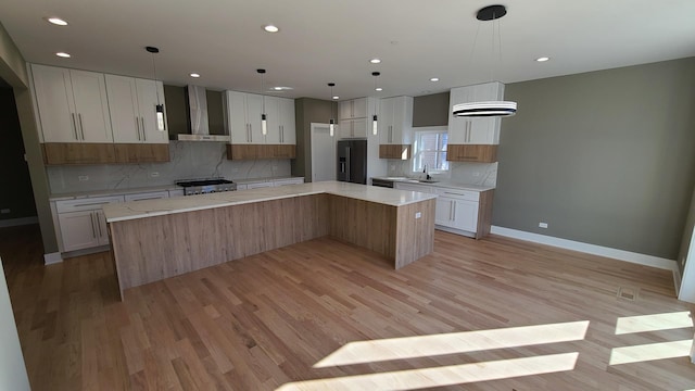 kitchen featuring decorative backsplash, black fridge with ice dispenser, light wood finished floors, a spacious island, and wall chimney range hood