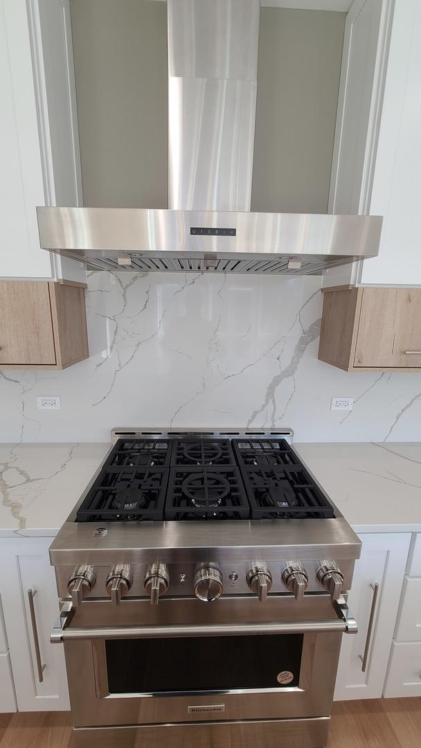 details with wall chimney range hood, white cabinetry, tasteful backsplash, and high end stainless steel range oven