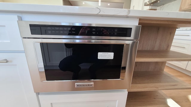 room details featuring white cabinets, light countertops, stainless steel oven, and wood finished floors