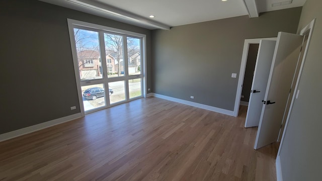 empty room with baseboards, beamed ceiling, and wood finished floors