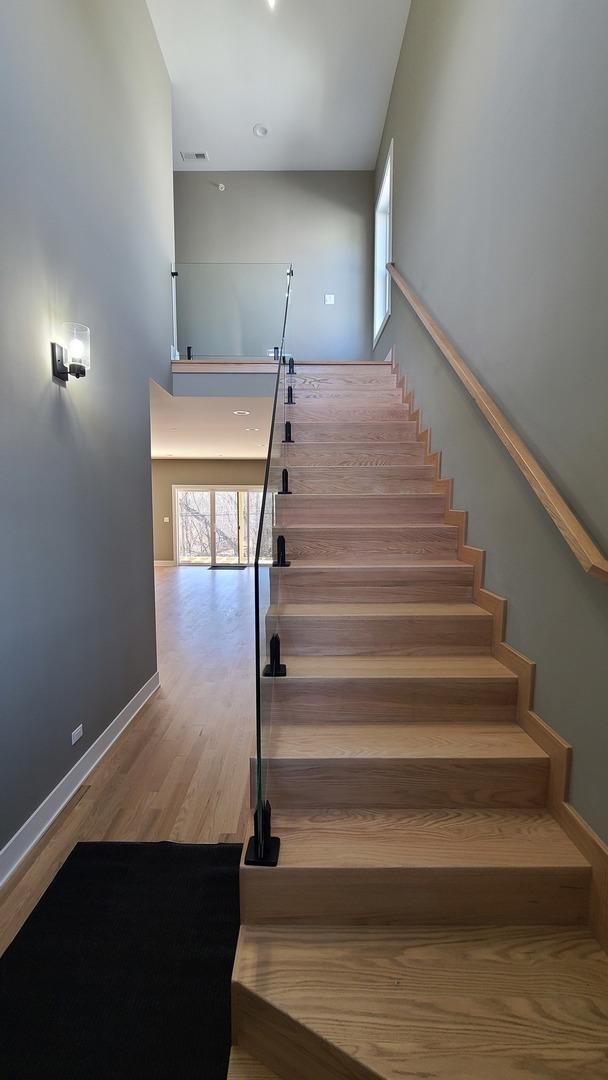 staircase with visible vents, wood finished floors, a towering ceiling, and a healthy amount of sunlight