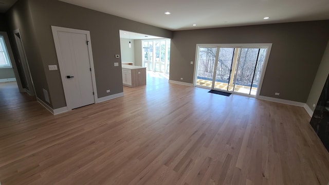 unfurnished living room featuring baseboards, a healthy amount of sunlight, recessed lighting, and light wood finished floors