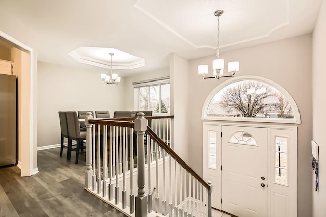 foyer entrance with baseboards, wood finished floors, an inviting chandelier, and a raised ceiling
