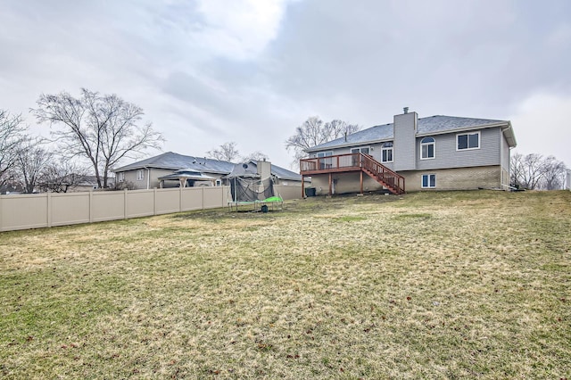 view of yard featuring a wooden deck, fence, stairway, and a trampoline