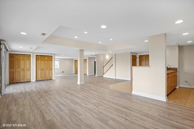 unfurnished living room featuring light wood-style floors, stairs, baseboards, recessed lighting, and a sink