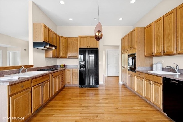 kitchen with black appliances, a sink, under cabinet range hood, light wood finished floors, and recessed lighting